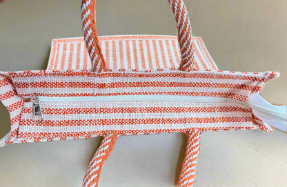 Orange and white striped bag with a zipper on a wooden surface.